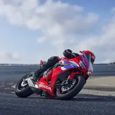 Motocyklista pochyla się na torze wyścigowym na czerwonym motocyklu Honda CBR650R.