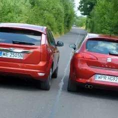 Dwa czerwone auta, Ford Focus i Seat Leon, jadą obok siebie. Wymijanie czy omijanie? Droga wąska, otoczona zielenią.