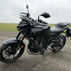 Czarny motocykl Yamaha MT-03 stoi na betonowej nawierzchni, gotowy do jazdy po zielonym polu.