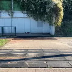 Przejście sugerowane dla pieszych obok torów tramwajowych. Na chodniku pod ścianą budynku stoją znicze.
