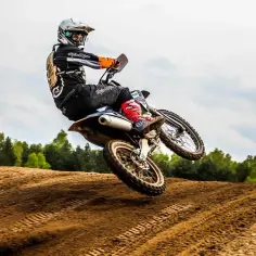 Motocyklista w kasku i stroju skacze na motocyklu po piaszczystym torze.