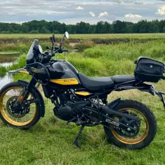 Czarny Royal Enfield Himalayan z żółtymi akcentami na tle łąki i rzeki. Gotowy na przygodę!