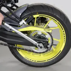 Dłoń używa klucza dynamometrycznego, by dokręcić śrubę przy tylnym kole motocykla z żółtą felgą.