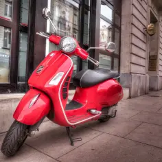 Czerwona Vespa na chodniku. Zastanawiasz się, ile kosztuje prawo jazdy AM?