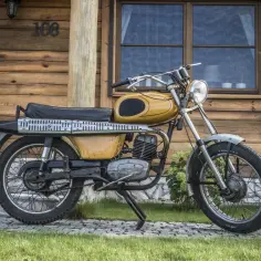 Żółty motorower WSK 175, z widocznymi danymi technicznymi na silniku, stoi przed drewnianym domem.