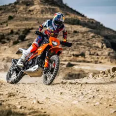 Motocyklista w pełnym rynsztunku śmiga pomarańczowym motocyklem po pustynnym terenie. Czy enduro można jeździć po ulicy? Ten sprzęt wygląda na gotowy na wszystko!
