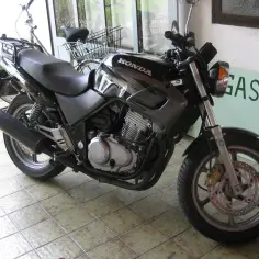 Czarny motocykl Honda na wybrukowanym podwórku, z zielonym napisem "GASTHAL" w tle.