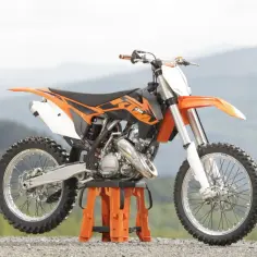 Pomarańczowy KTM SX 125 na stojaku. Ten motocykl terenowy, znany z mocy, ma silnik o pojemności 125 cm3, który generuje ok. 38 KM.