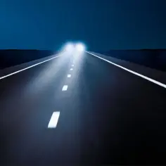Nocna droga z białymi pasami i oślepiającymi światłami drogowymi pojazdu zbliżającego się z naprzeciwka.
