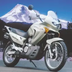 Jasnosrebrny motocykl Honda Transalp 650 gotowy na przygodę na tle ośnieżonej góry.