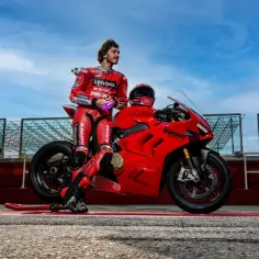 Motocyklista w czerwonym kombinezonie opiera się o swoją czerwoną Ducati Panigale V4 na torze wyścigowym.