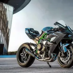 Czarny motocykl Kawasaki H2R z zielonymi akcentami stoi przed nowoczesnym budynkiem.