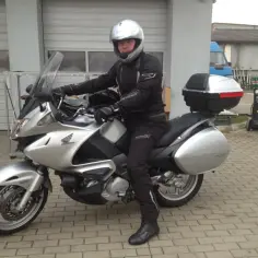 Motocyklista w kasku siedzi na srebrnym Honda Deauville, gotowy do podróży.