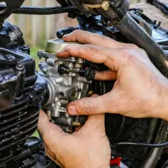 Dłonie mechanika regulują gaźnik motocykla, kluczowy element dla prawidłowego symbolu ssania i pracy silnika.