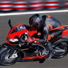 Motocyklista w kombinezonie śmiga na torze na czerwono-czarnej Aprilia RS4.