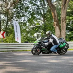 Motocyklista na czarnym Kawasaki Ninja H2 z zielonymi akcentami mknie po drodze, otoczony drzewami.