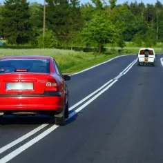 Czerwony Opel próbuje wyprzedzanie na podwójnej ciągłej, mandat murowany. Biały bus jedzie z przodu.