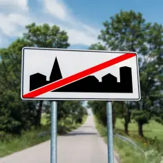 Znak d42: koniec obszaru zabudowany. Droga prowadzi przez zielone krajobrazy, a znak informuje o opuszczeniu miasta.