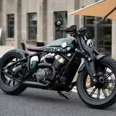 Stylowy, zielony motocykl typu **yamaha cruiser** z brązowym siedzeniem i czarnymi felgami, zaparkowany na ulicy.