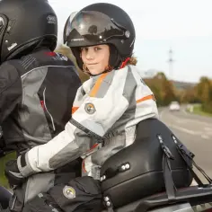 Dziecko w kasku i kurtce motocyklowej, bezpiecznie przewożone na motocyklu przez osobę dorosłą.