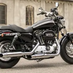 Czarny motocykl Harley Sportster 1200 z chromowanymi elementami, zaparkowany przed budynkiem.