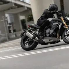 Motocyklista w kasku i skórzanej kurtce dosiada czarnego Triumph Speed Triple, pochylony w zakręcie na miejskiej ulicy.