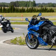Błękitny motocykl Suzuki na torze wyścigowym, obok inny motocyklista w ruchu. Różne modele Suzuki to marzenie każdego fana dwóch kółek.