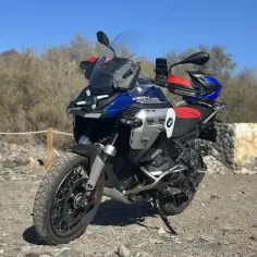 Nowy BMW R1300GS gotowy na przygodę na pustynnych drogach. Niebiesko-czerwono-srebrny motocykl z kaskiem na siedzeniu.