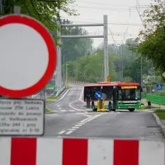 Znak b1 zakazu wjazdu, autobus miejski na drodze, w tle most i linie energetyczne.