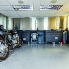 Warsztat z motocyklem i narzędziami. Widać tu m.in. układ dolotowy silnika, stoły warsztatowe i szafki z narzędziami.