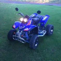 Niebieski Yamaha Warrior 350 z błyszczącymi światłami stoi na trawie, gotowy na przygodę.