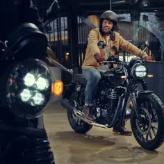 Mężczyzna w kasku i brązowej kurtce siedzi na czarnym motocyklu Honda GB350S. Zbliżenie na przednie światło.