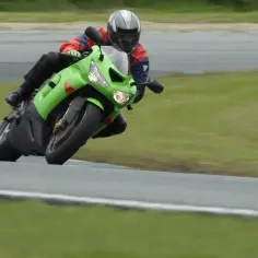 Motocyklista w zielonym stroju wykonuje ostry zakręt, stosując technikę przeciwskrętu na torze wyścigowym.