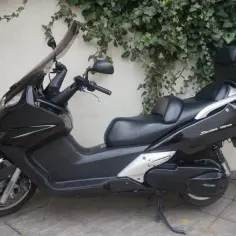 Czarny skuter Honda Silver Wing 600 z kuferkiem na bagaż, zaparkowany przy ścianie porośniętej bluszczem.