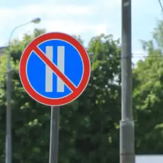 Znak B37 zakazujący postoju. Dwa pionowe białe paski na niebieskim tle, przekreślone czerwoną linią.