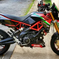 Sportowy motocykl Aprilia Dorsoduro 750 w kolorach włoskiej flagi, z czerwonym stelażem i złotym zawieszeniem, gotowy do jazdy.