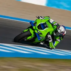 Zielony motocykl Kawasaki ZX-9R Ninja na torze wyścigowym, pochylony w zakręcie.