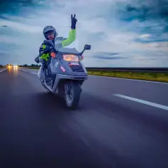Rowerzysta na motorowerze, pozdrawiający znakiem pokoju, jedzie autostradą. Czy można jeździć motorowerem na dowód? Tak, jeśli masz odpowiednie uprawnienia.