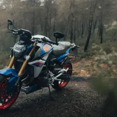 Niebiesko-biały motocykl BMW F900R z czerwonymi felgami na tle jesiennego lasu.