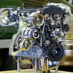 Silnik DOHC z widocznymi paskami i kołami zębatymi, prezentowany na tle zielonego pojazdu.