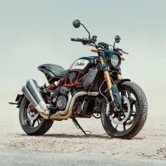 Stojący na piasku motocykl Indian FTR 1200 z podwójnym wydechem i złotym zawieszeniem.