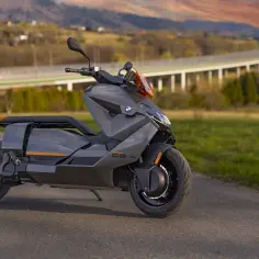Szary skuter elektryczny BMW CE 04 stoi na drodze z widokiem na most i wzgórza w tle.
