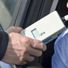 Policjant bada kierowcę alkomatem. Za jazdę po alkoholu, np. z wynikiem 1 promil, prawo jazdy jest zabierane.