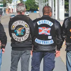 Czterech mężczyzn w kamizelkach z naszywkami klubów motocyklowych MC: Hells Angels, Nomads, Rebels, Bandidos. MC to skrót od Motorcycle Club.