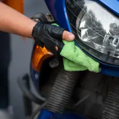 Ręka w rękawiczce poleruje plastikowy reflektor motocykla zieloną ściereczką, przywracając mu blask.