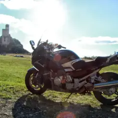 Motocykl na trawie, w tle ruiny zamku na skale. Idealne miejsce na podróż szlakiem Orlich Gniazd.
