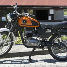 Klasyczny motocykl WSK 125, z pomarańczowym bakiem i napisem "125", gotowy do drogi.