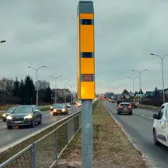 Żółty słup z urządzeniem multaradar cd. monitoruje ruch na drodze. Samochody jadą w obu kierunkach.
