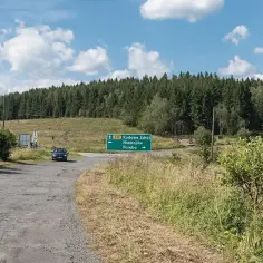 Droga w Sudetach, z zielonym znakiem kierującym do Kudowy Zdroju. Las i polna droga tworzą malowniczy krajobraz.