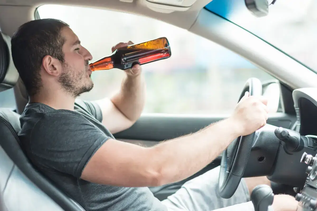 Mężczyzna pije piwo za kierownicą, ignorując dopuszczalną ilość alkoholu.